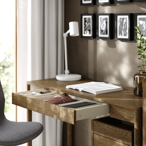 Wooden desk with an open drawer, containing notebooks and a lamp on top.