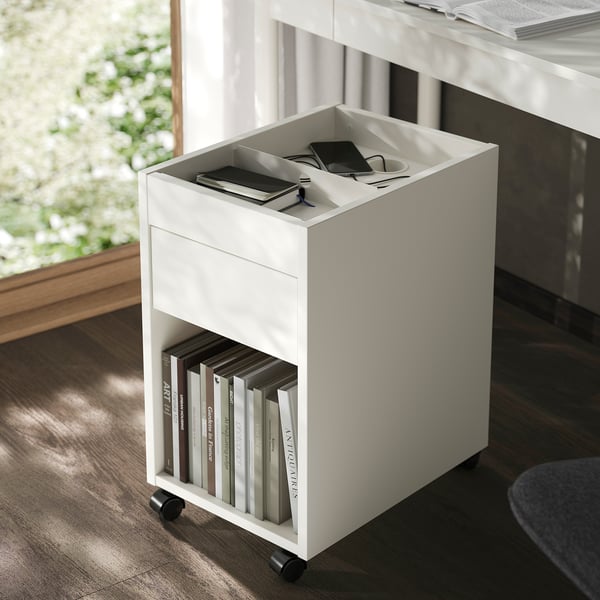 Small white mobile storage unit with drawer, holding books below and tech items on top, ideal for organising office space.