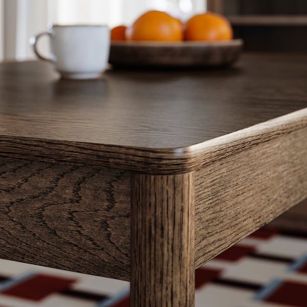 Wooden table with smooth, rounded edges. Visible grain patterns and natural colour variations. Coffee cup and oranges on surface.