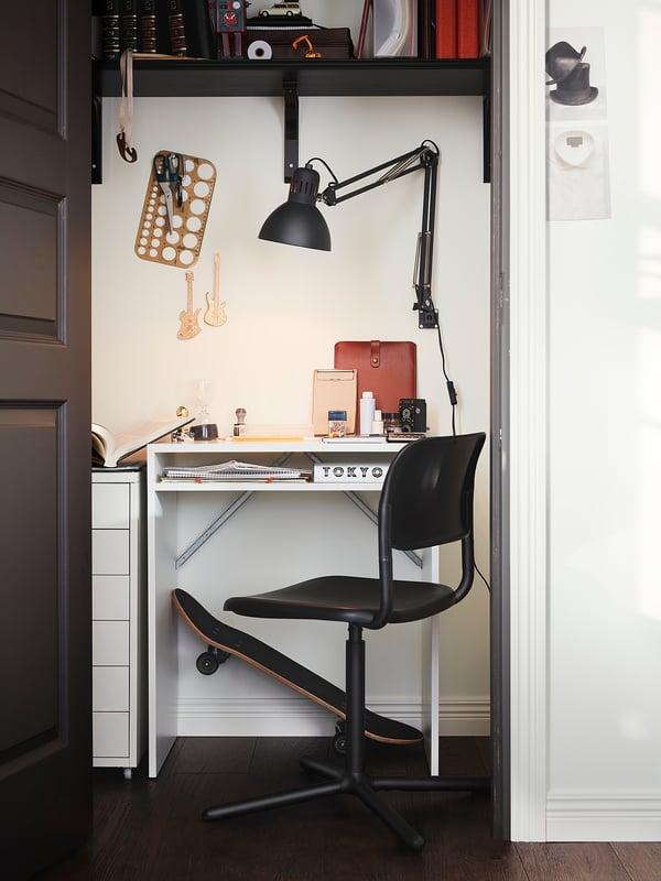 Compact home office: white desk, black chair, wall lamp, skateboard, guitar decor.