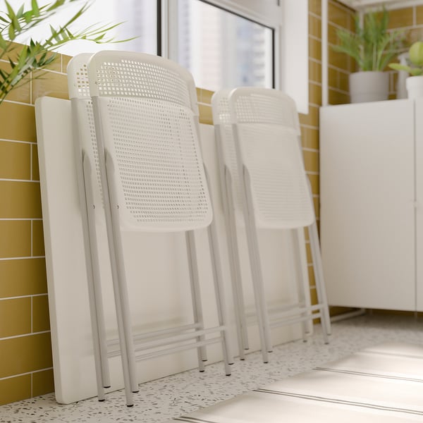 Three white plastic TORPARÖ bar stools folded against a yellow-tiled wall. Modern, stackable design, ideal for small spaces.