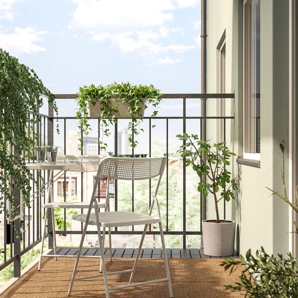 Cosy balcony with TORPARÖ chairs and table on small rug, two green plants, beige wall with window.