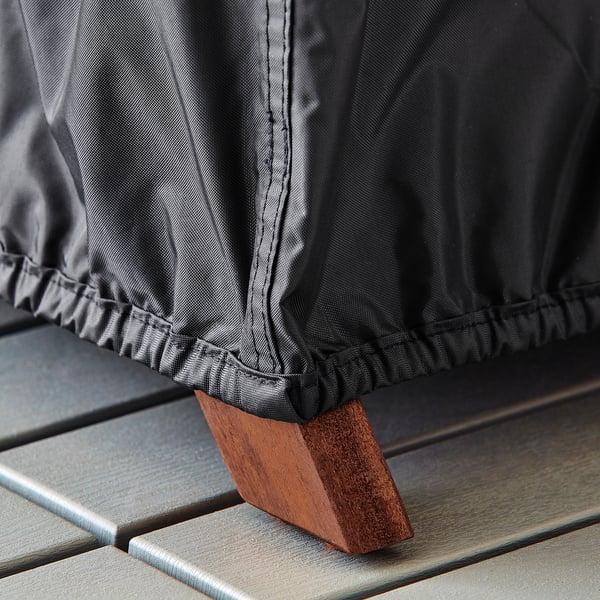 Black waterproof outdoor furniture cover with elastic hem, secured on wooden bench leg.