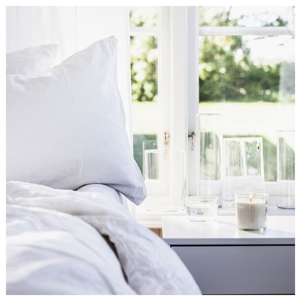 Cosy bedroom with white pillows, candle, and water glass near window.