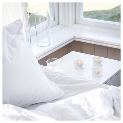 White bedroom with candles; crisp, clean décor. Lighted candles on window sill, soft ambiance.