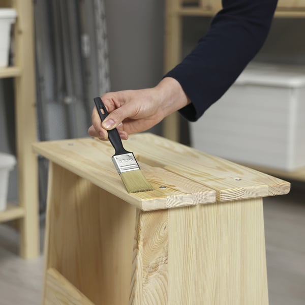 A person applies TRIXIG oil to a wooden shelf, enhancing its sheen and protection.