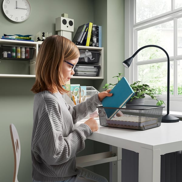 Person organises items in desks mesh box with lamp and plant.