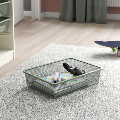 Metal mesh storage box on beige carpet, containing gaming controllers and a remote, perfect for organising gadgets in a TROFAST frame.