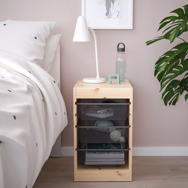 Wooden TROFAST storage by bed with lamp, bottle & plants.