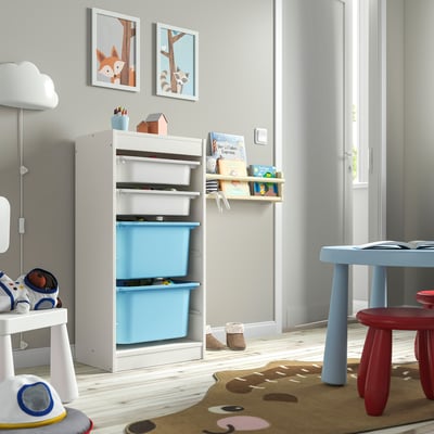 Kids storage unit TROFAST in white & blue. Plastic bins, wooden frame, low & accessible. Near small table, rug, & toys.