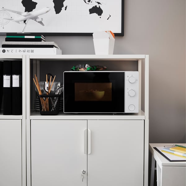 Small white TROTTEN microwave on shelving, surrounded by kitchen utensils and binders.
