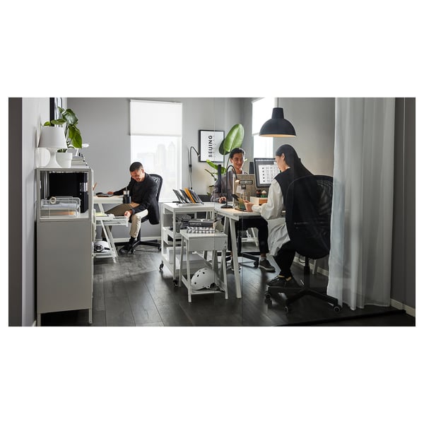 Three people in modern office with white TROTTEN desks, stainless steel legs, and white chairs, working under black pendant lamps.