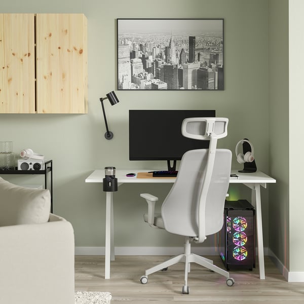Minimalist home office setup with white TROTTEN desk and chair, black monitor, wooden shelf, and cityscape wall art.