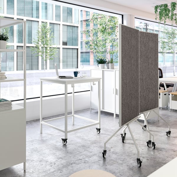 Modern office space with white TROTTEN tables, one with a laptop, and mobile blackboard on wheels.