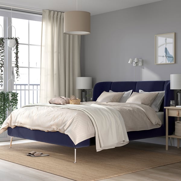 Modern bedroom with TUFJORD bed in blue, large windows, soft linens, and hanging plant. Cosy, relaxation-focused design.