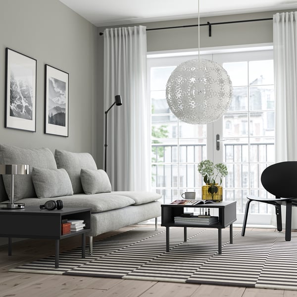 Modern living room with grey sofa, black coffee table, striped rug, floor lamp, large pendant light, and balcony view.