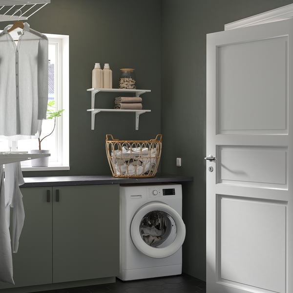 Modern laundry room with white washing machine, green cabinets, laundry basket, and white door.
