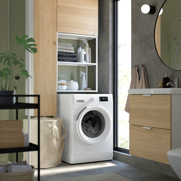Modern laundry area with white washing machine, beech cabinet, and glass door.