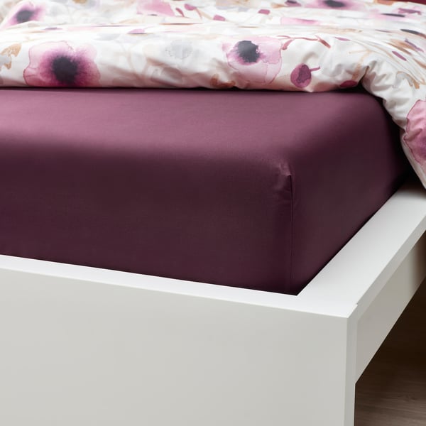 A bed with a burgundy fitted sheet on a white frame. The sheet has elastic edges to fit a thick mattress.