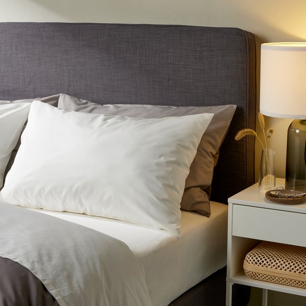Cozy bedroom with dove gray ULLVIDE bedding, large bed, lit lamp, and small bedside table with bench.