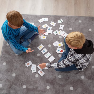 Two kids playing with letter/number cards on rug.