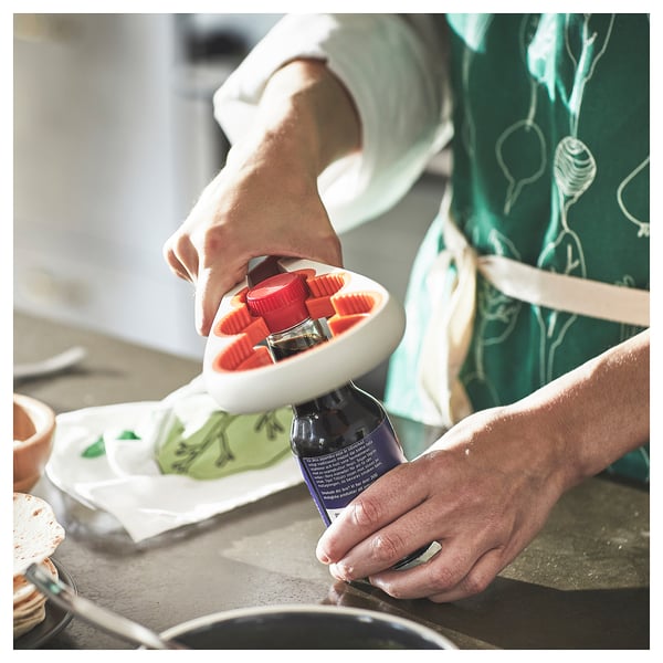 Person opens red jar with silicone grip opener over kitchen counter with food.