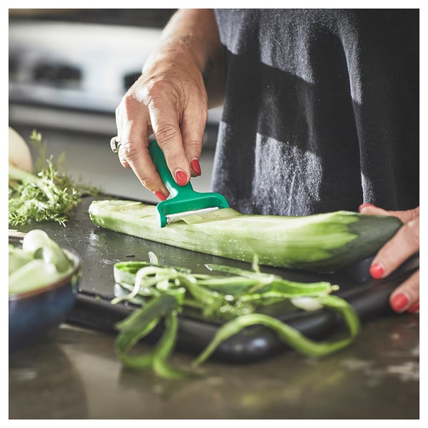 Person peeling cucumber with green UPPFYLLD peeler. Kitchen counter with sliced cucumber.