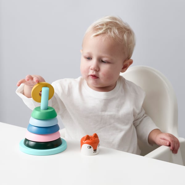 A young child plays with a stackable ring toy on a high chair, improving motor skills and learning shapes and colours.