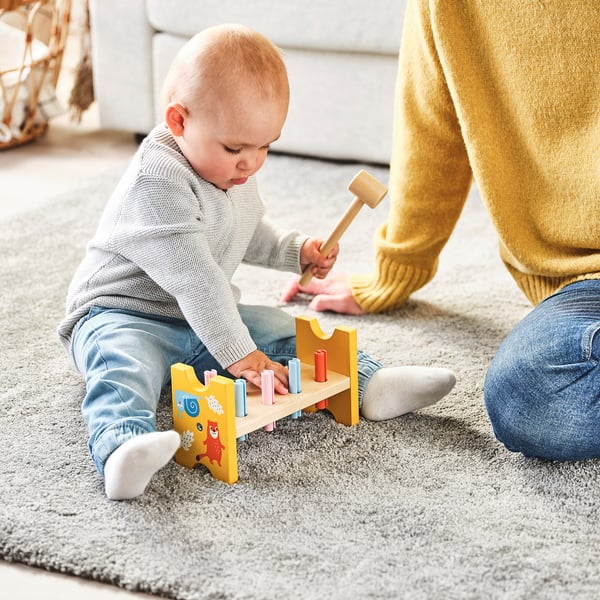 Baby playing with UPPSTÅ hammering toy, pounding plugs, adult guiding nearby.