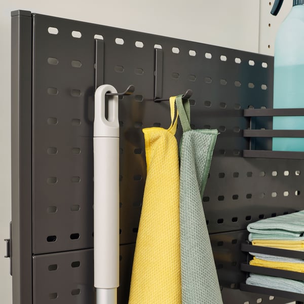 Organised cleaning supplies on hooks and shelves. Includes a brush, yellow cloth, green cloth, and stack of cloths, mounted on a pegboard panel.