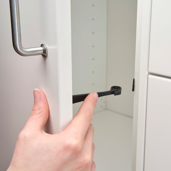 A hand attaches a black cabinet lock to a white cabinet, enhancing child safety.