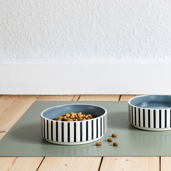 Two striped stoneware pet bowls on a green mat, one filled with dog food, demonstrating its use for pet feeding.