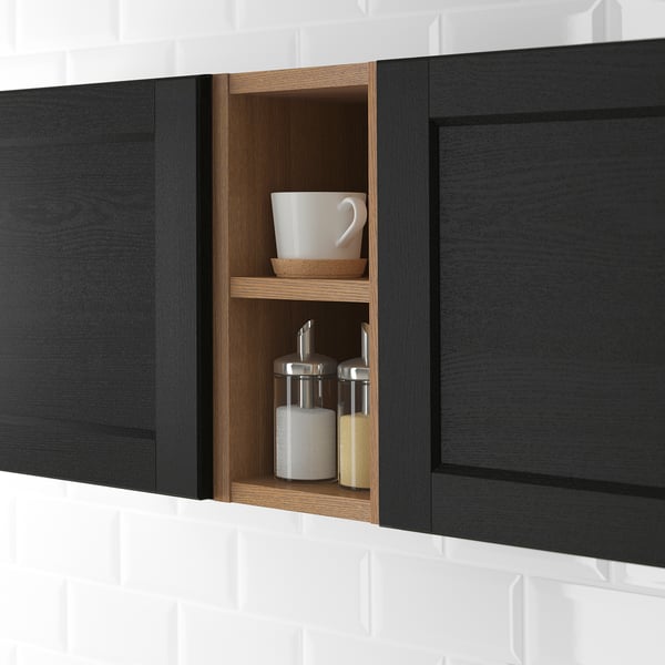 Black kitchen cabinet with open section, holding a white mug, small bowl, and two spice jars on light wood shelves.