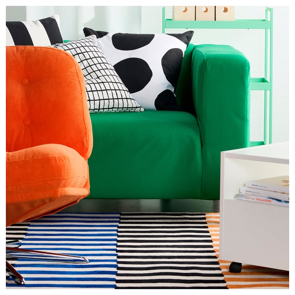 Bright modern room with green sofa, orange chair, and colourful striped rug.
