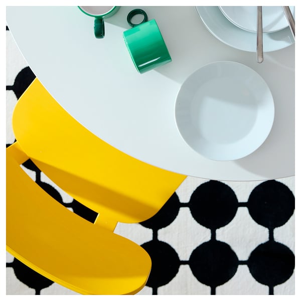 Bright yellow modern chair near white table with bowls, green objects; black & white geometric floor design.