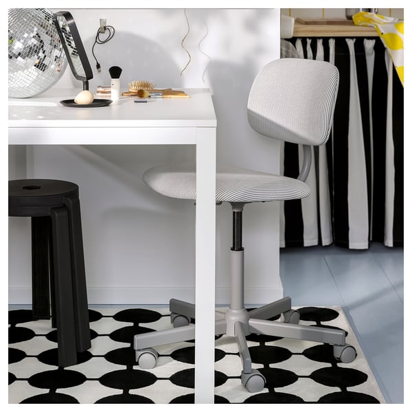 A VÄNDPLATS black and white rug with a circular pattern under a modern desk and a grey chair with wheels.