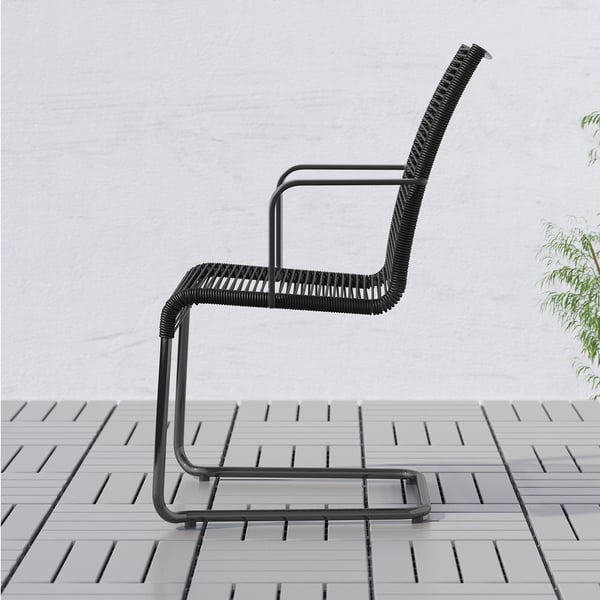 Black modern outdoor chair with high back and armrests for comfort, placed on tiled patio.