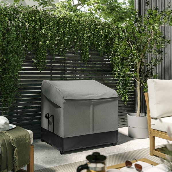 Gray VÄTTERSÖ outdoor storage box with durable fabric, holding cushions, surrounded by plants and furniture.