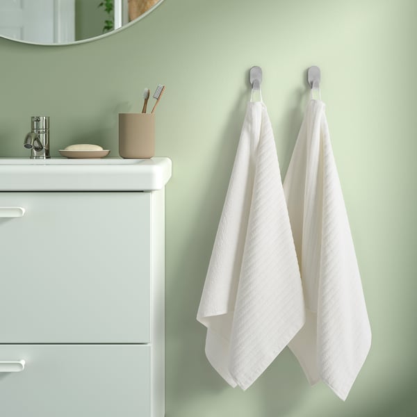 Two VÅGSJÖN towels hang on hooks by a green wall vanity with soap and toothbrushes.