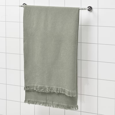 Green VALLASÅN towel on shower rack. Rectangular, textured, fringed ends.