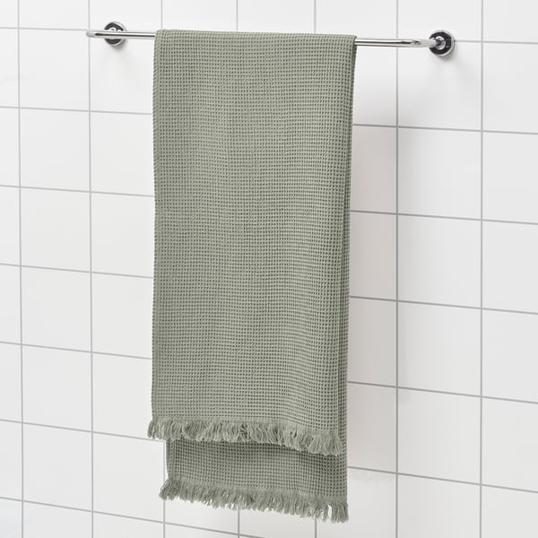 Green VALLASÅN towel on silver rod against white tiles, textured with fringe.