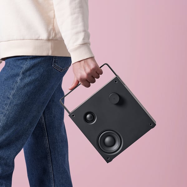 Person holding a black VAPPEBY bluetooth speaker. The speaker has a handle and two visible speakers, ready for audio playback.