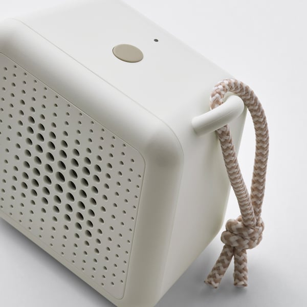 Compact, portable speaker with braided handle, smooth finish and numerous holes for audio output.