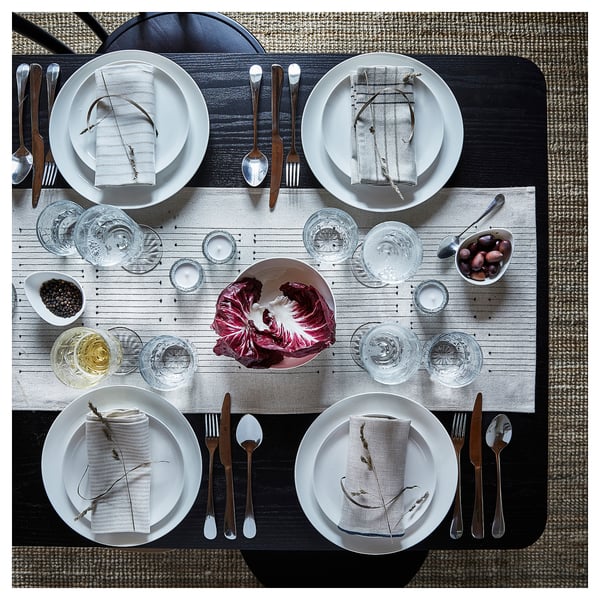 Elegant table set with VÅRARV runner, white plates, wooden cutlery. Centred red cabbage, glasses, olive bowl. Patterned napkins, subtle tassels.