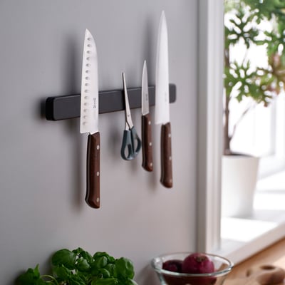 Magnetic knife rack holds multiple knives, scissors, and a peeler on a wall, keeping countertops clear.