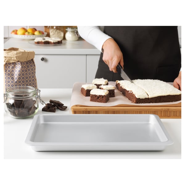Person slices frosted brownies on a bamboo cutting board. A white baking tray sits nearby on the countertop.