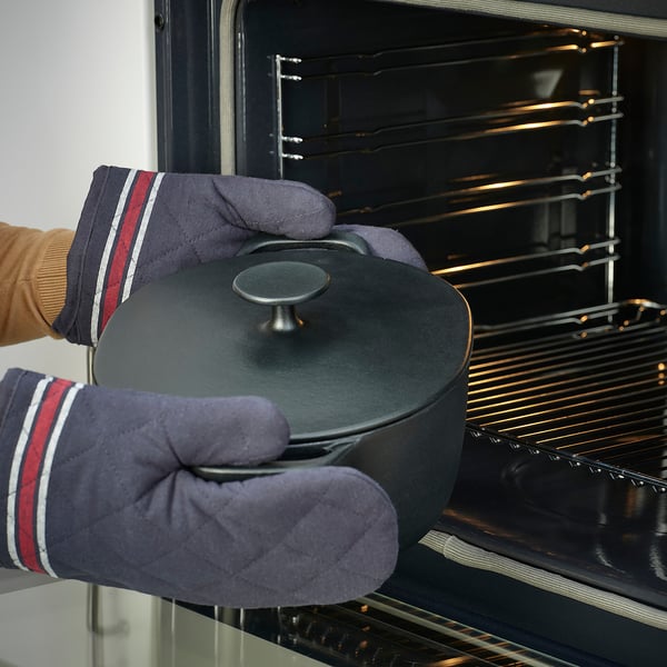Hands in oven mitts carefully place an enamelled cast iron casserole into an oven, showcasing even heat distribution.