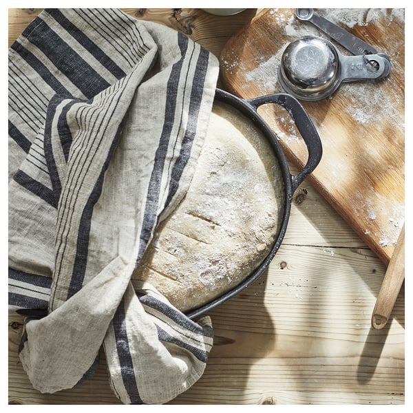 VARDAGEN black cast-iron pan on wooden surface. Covered with striped cloth. Other kitchen tools nearby.