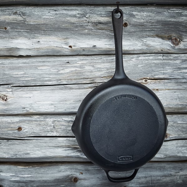 Black cast iron frying pan hangs on rustic wooden wall. Two handles, ideal for stove and oven use.