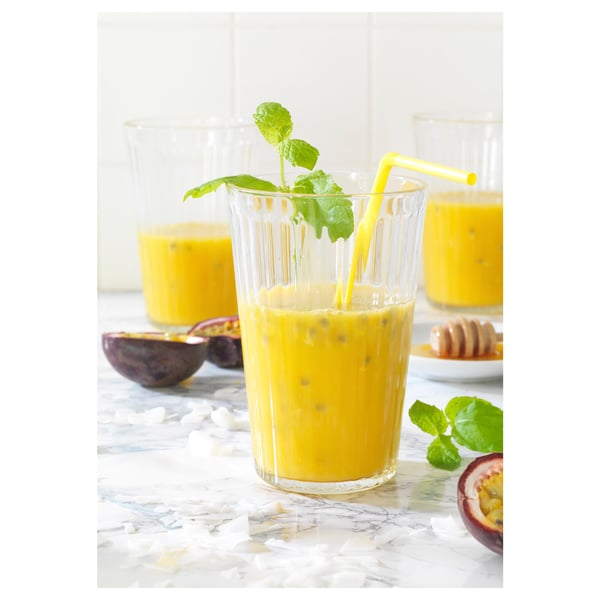 Glasses of yellow smoothie on marble, garnished with leaves, straws, passion fruits, and coconut.